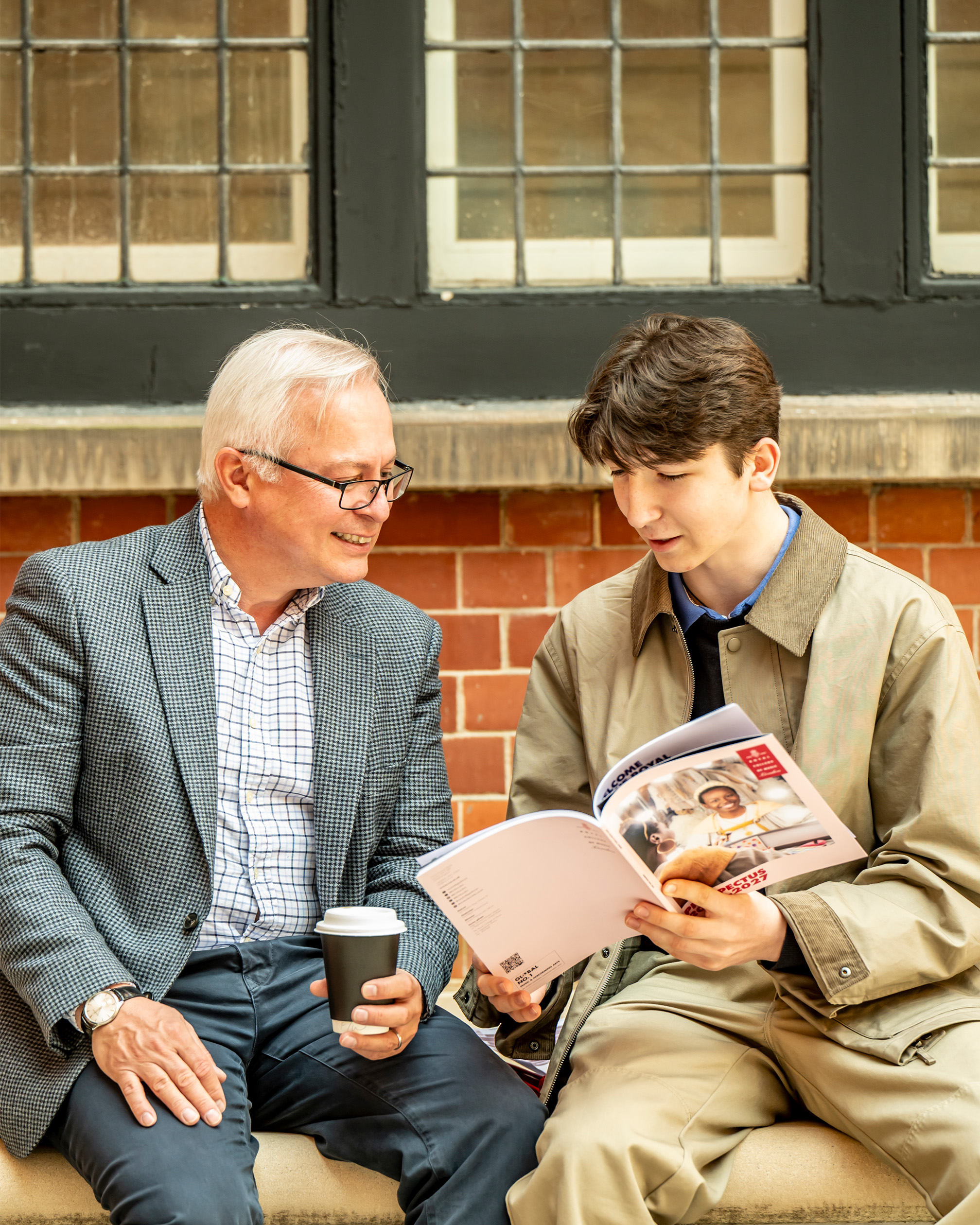 An older man and a young man, looking at the RCM prospectus, smiling.